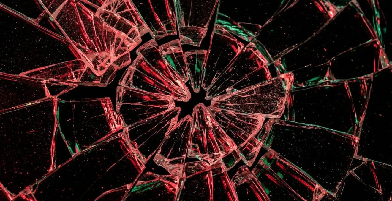 Abstract representation of a shattered glass surface, with red and green light reflecting off the pieces, symbolizing portfolio deterioration from overtrading.